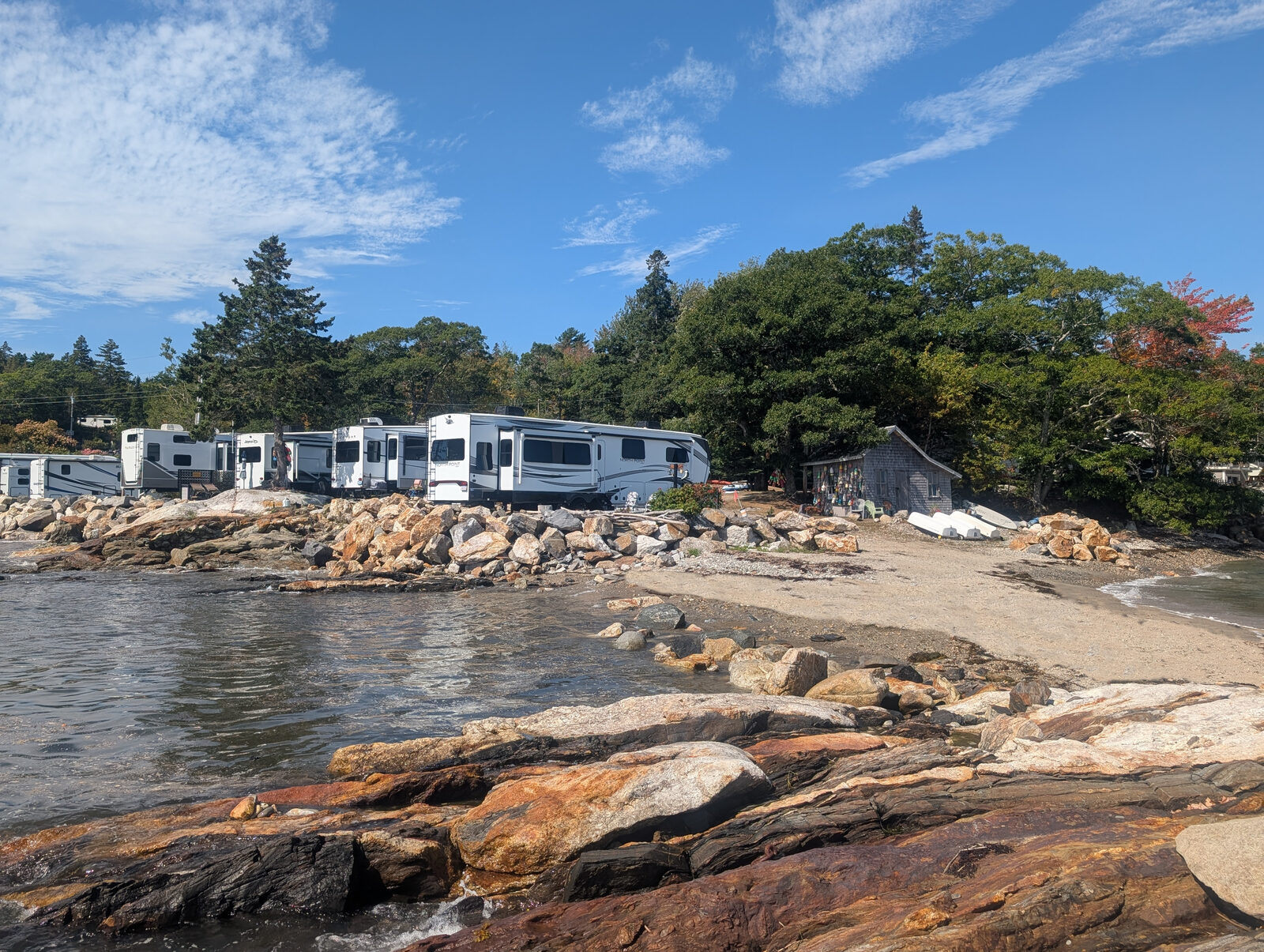 Rocky shoreline at Gray Homestead with RVs parked along the water and a sandy beach beyond