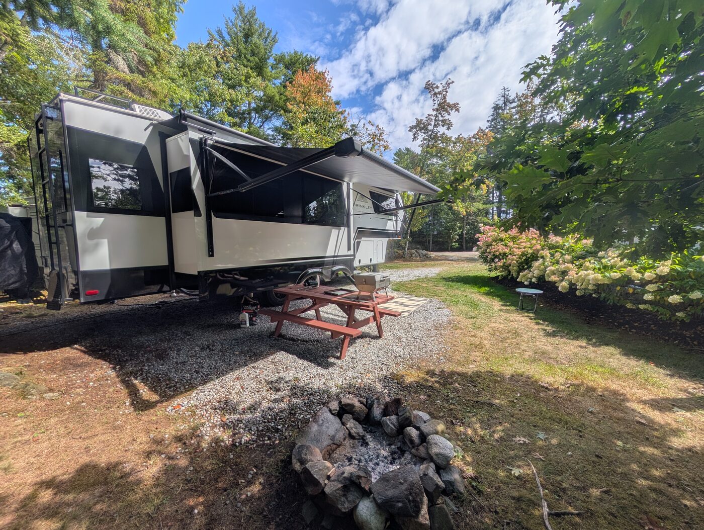 Site 5 fifth-wheel RV with awning extended over a picnic table and fire pit